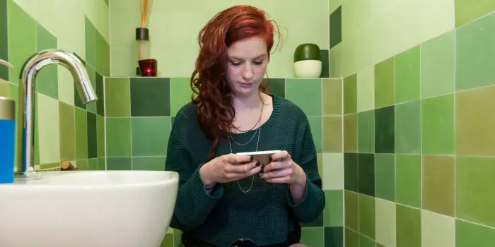 Young woman checking social media on the toilet