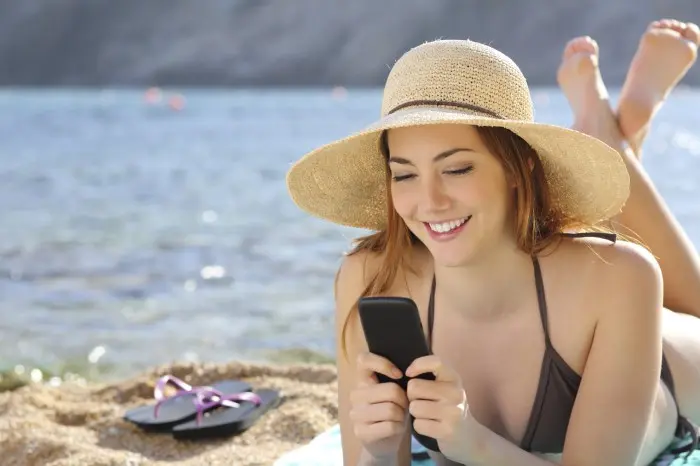 Woman on the beach texting a smart phone in summer with the sea in the background